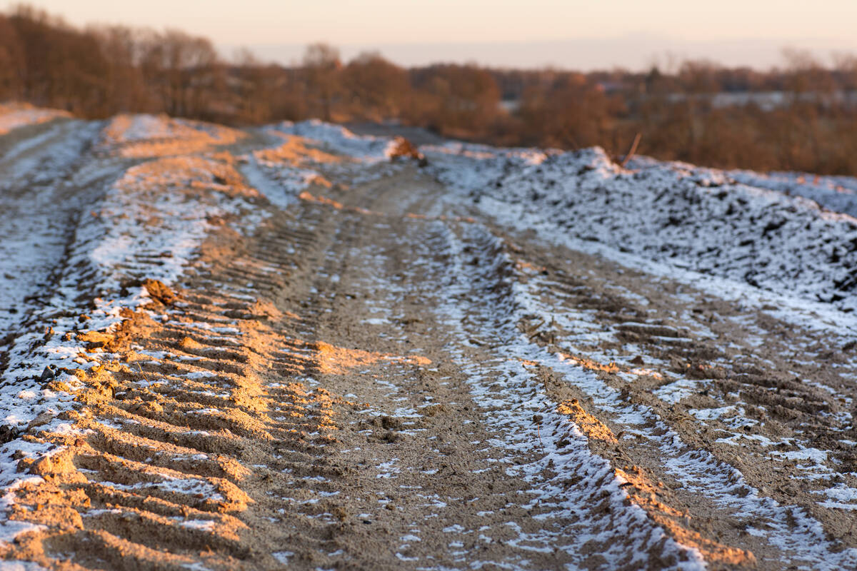 Traktorspuren im Sand eines winterlichen Feldes, die von der tief stehenden Nachmittagssonne touchiert werden